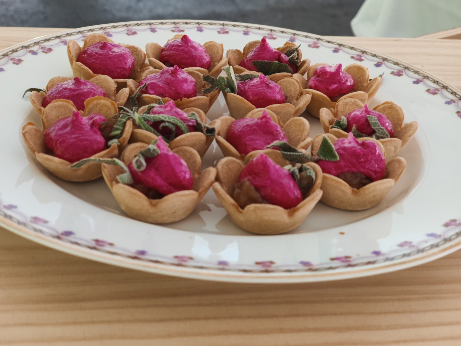 Pink beet-mousse tartlets garnished with herbs in bite-size pastry shells
