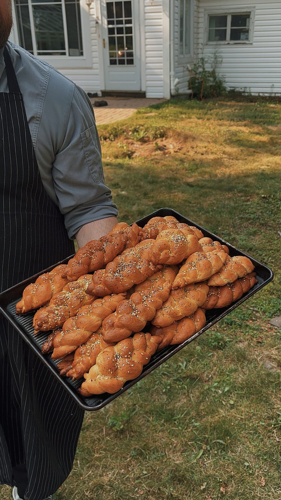 A tray of golden braided challah carried by a staff member in an apron